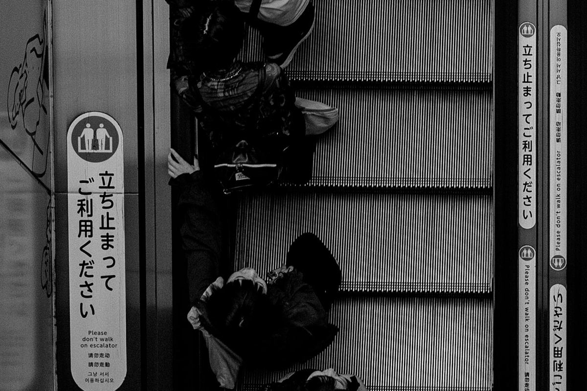 An escalator in Japan. The sign reads "Please stand still" (立ち止まってご利用ください).
